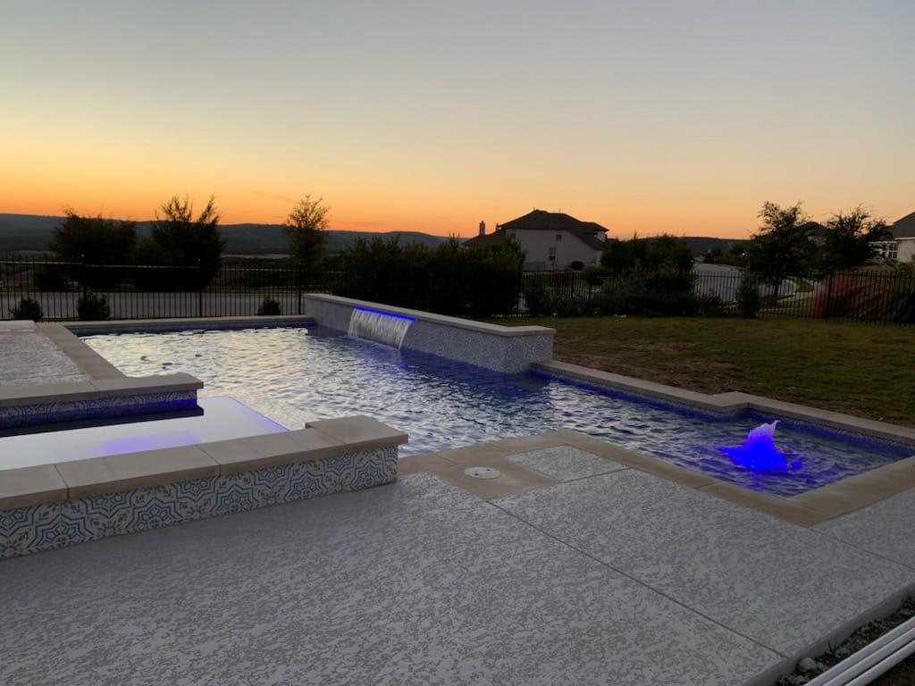 Twilight pool and spa with blue lighting overlooking the Hill Country